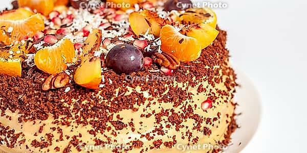 This delicious-looking cake, adorned with fresh fruits and nuts, is served on a white plate. The sweet treat is ideal for celebrations [IBR124491546]