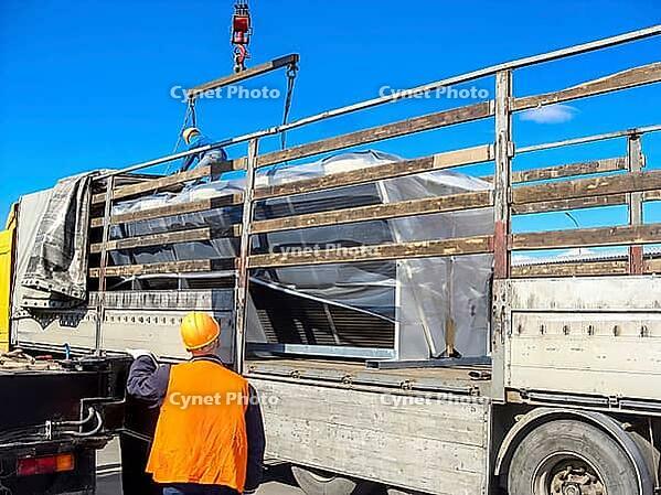 Two workers load large condenser units onto a flatbed truck, securing them for transportation on a bright, sunny day [IBR124491554]