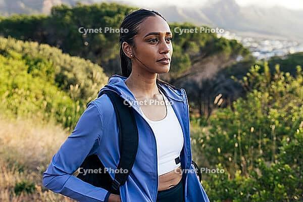 Portrait of young female in sportswear with backpack standing outdoors at sunset [IBR124491568]