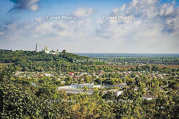 A scenic view of a town with a golden-domed church on a hilltop, under a blue sky with fluffy clouds [IBR124491571]