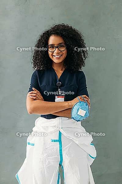 Smiling nurse standing at wall with crossed arms and holding respirator [IBR124491572]