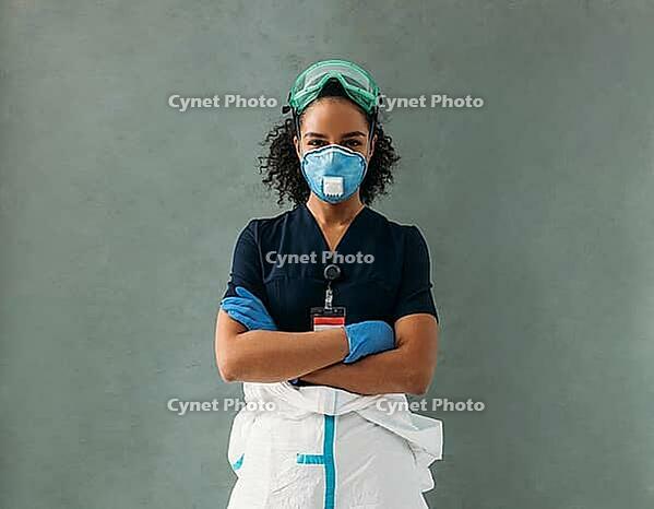 Confident nurse wearing protective eyeglasses, gloves, suit, and respirator looking at camera [IBR124491579]