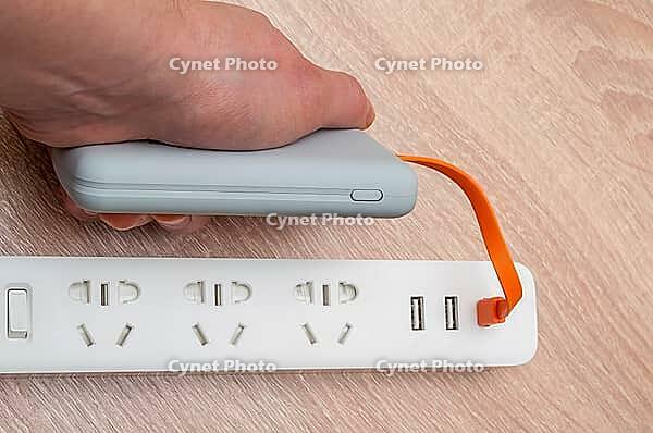A hand plugging a portable power bank into a power strip. Modern tech to charge electronics [IBR124491589]