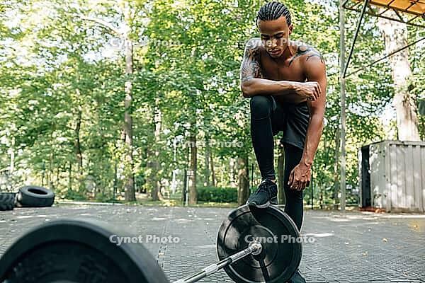Young sportsman resting after a workout. Bare-chested man standing at the barbell [IBR124491595]