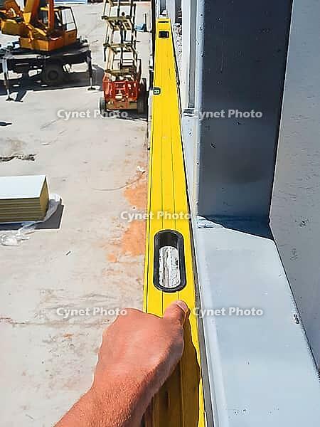 A construction worker uses a spirit level to ensure a structure is perfectly aligned, with construction equipment visible in the background [IBR124491614]