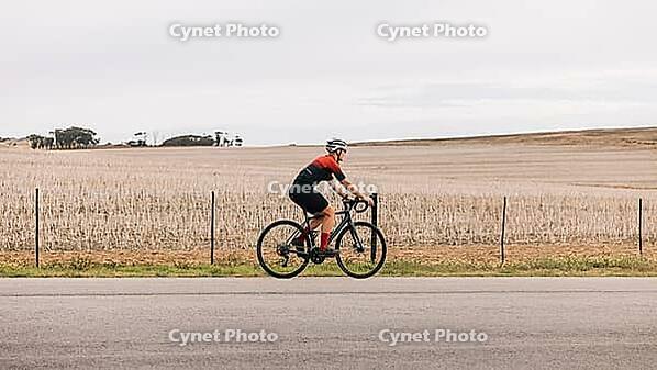 Woman cyclist exercising outdoors on road bike against agriculture field [IBR124491616]