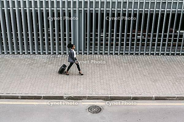 High angle view of businesswoman walking with suitcase near parking garage [IBR124491623]