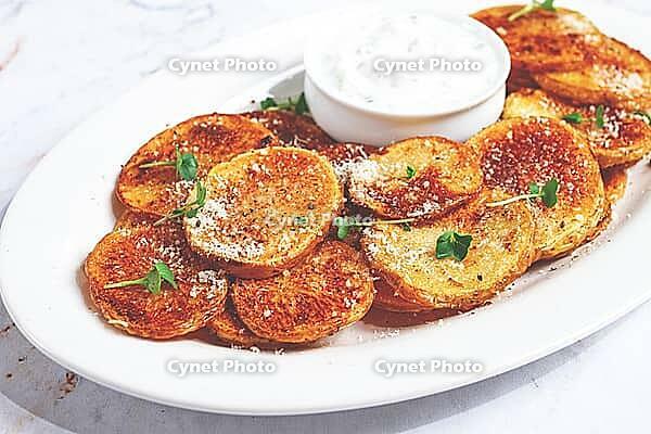 Crispy potato slices, with parmesan cheese and spices, baked in the oven, with zajiki sauce, on a white plate [IBR124491628]