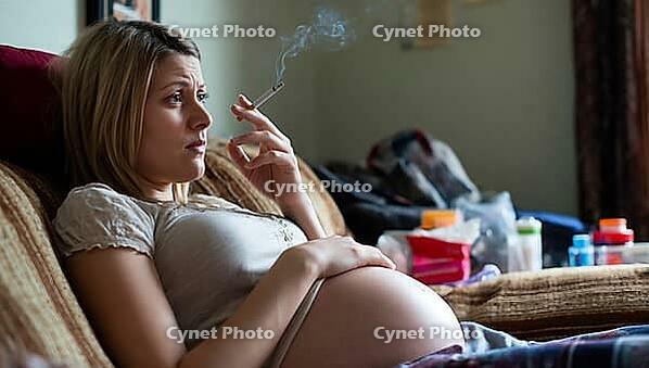 Pregnant woman smokes on a sofa, appears thoughtful and uncertain, health risk from smoking, symbolic image, AI generated [IBR124494032]