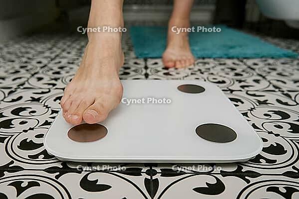 Bare feet woman checking her weight on weighing scales in bathroom. Female measuring her weight using digital scales on floor [IBR124497420]