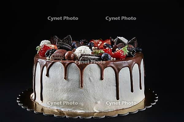 Birthday cake on dark background with copy space. Close up of cake decorated with fresh berries and chocolate sweets on dark background. Delicious dessert for party [IBR124497433]