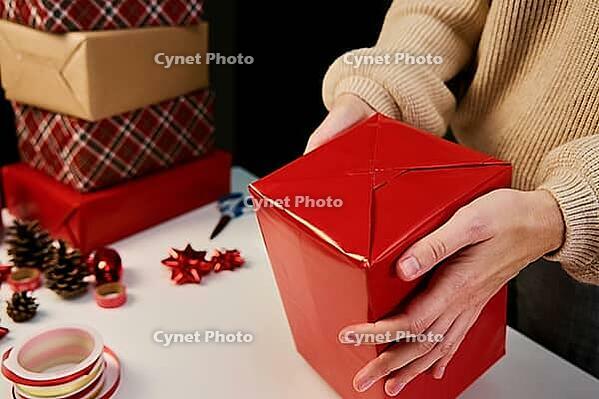 Woman in warm sweater packaging gift box with craft paper. Present for holiday event. Surprise for christmas party [IBR124497435]
