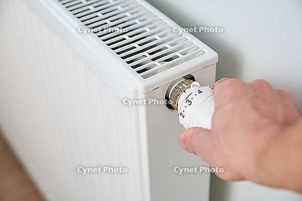 Hand adjusting temperature on heating radiator thermostat, Turning heat radiator knob to control heat in home [IBR124497442]