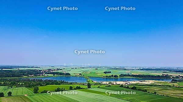 Windmill turbine generator against blue sky in countryside with green fields and lake, Concept of clean, renewable, sustainable, alternative energy [IBR124497448]