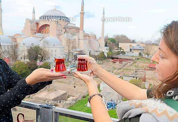 Hands of tourists with tradituional tea cai drink on background of the hagia sophia cathedral church, Istanbul Turkey [IBR124497457]