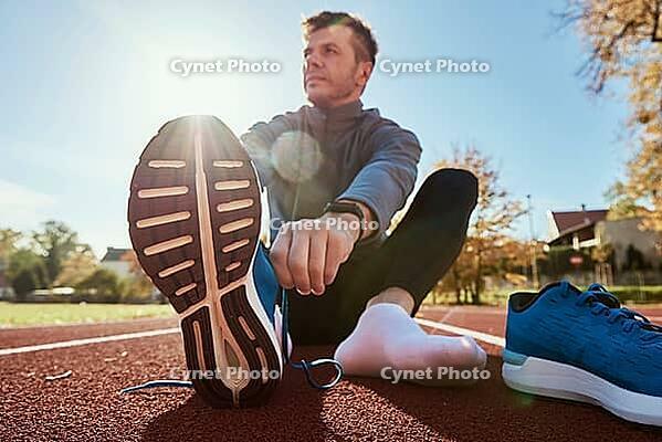 Male runner in blue sneakers get ready for run at stadium track, close up. Male hands tying on sport sneakers for jogging. Fitness and healthy lifestyle concept [IBR124497467]