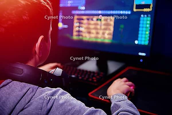 Teenager boy play computer video game in dark room, use neon colored rgb mechanical keyboard, workplace for cybersport gaming, children gaming addiction [IBR124497489]