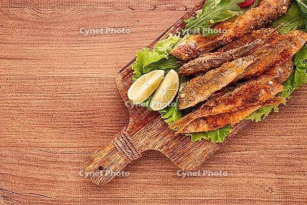 Fried crispy red mullet fish, on a wooden chopping board, with lime, no people [IBR124552169]