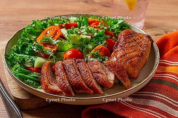 Delicious grilled duck breast served with fresh garden salad and cherry tomatoes at a rustic dining table [IBR124552172]