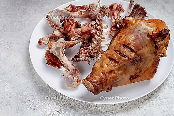 Roast pork head, with remnants of bones and meat, on a white platter, no people, close-up [IBR124552184]