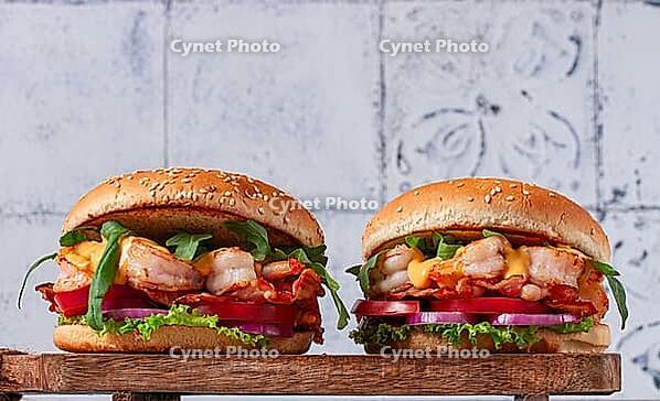 Two shrimp burgers and buns with sesame seeds, bacon, lettuce, tomatoes and onions, On a wooden board [IBR124552185]