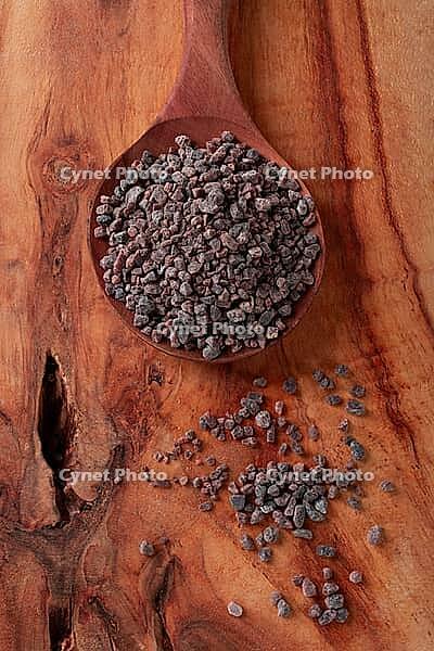 Crystals of black salt, on a wooden spoon, laid out on a wooden surface, top view [IBR124552201]