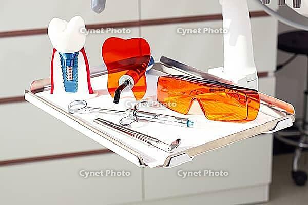 On the tray are various dental instruments, a model dental implant and bright orange safety glasses, ready for use in clinical dental settings [IBR124552206]