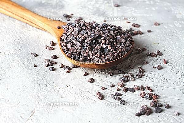 Crystals of black salt, on a wooden spoon, on a light surface, top view [IBR124552207]