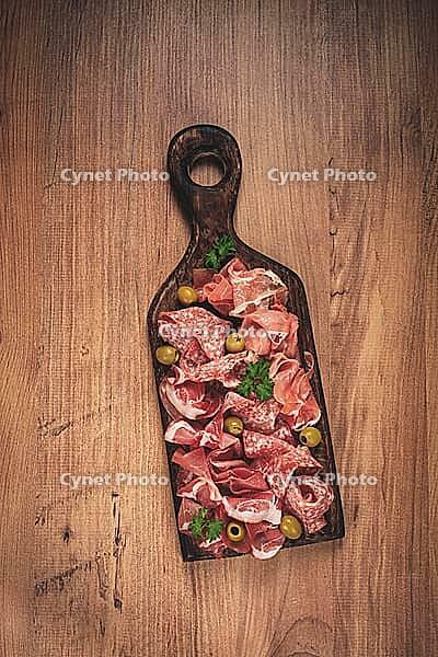 Assortment, sliced meat appetizer, prosciutto, salami and ham, with olives, on a wooden board, breakfast, top view, close-up, no people [IBR124552208]