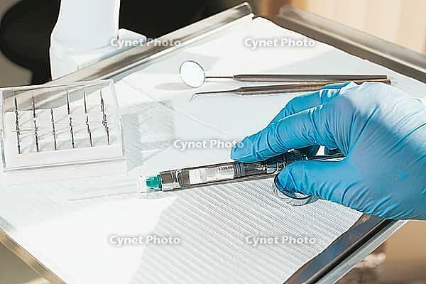 The dentist's hand, in a blue glove, holds a carpal syringe on a tray, ready for a medical procedure [IBR124552220]