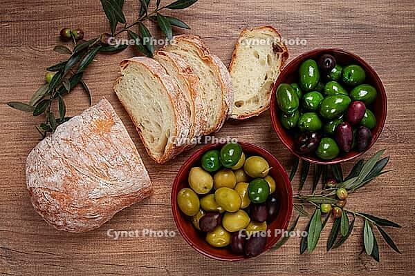 A mixture of olives, varieties of Halkidiki, Verdi giganti and Kalamata, in a bowl, with sliced ciabata bread, top view, no people [IBR124552231]
