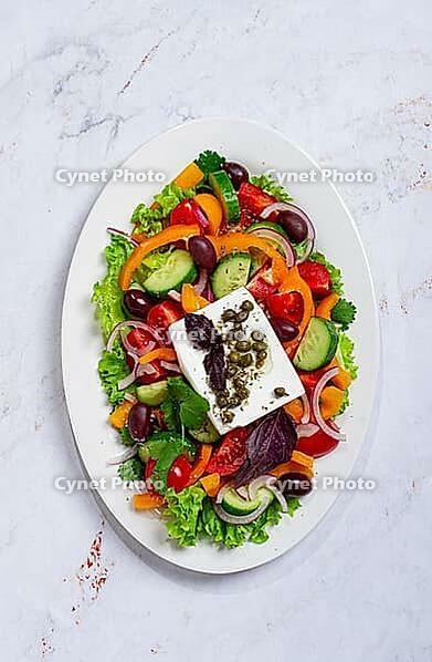 This dish features a salad made with a mix of lettuce, peppers, cucumbers, red onion, and olives. It is topped with feta cheese and capers [IBR124552235]