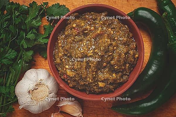 Green adjika, in a clay bowl, Georgian sauce, with ingredients on a wooden board, top view, no people [IBR124552250]