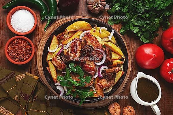 Ojakhuri, fried meat with potatoes, in ketsi, on a wooden table, Georgian cuisine, against a background of fresh ingredients [IBR124556502]