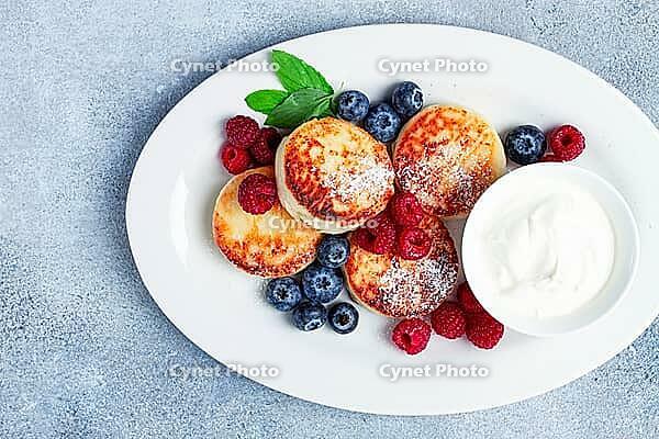Breakfast, cottage cheese cakes, with fresh berries, and sour cream, top view, close-up, no people [IBR124585338]