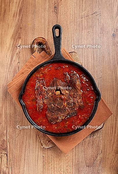 Fried steak, veal neck on the bone, stewed with vegetables, in tomato sauce, cooking meat, in a cast-iron frying pan, top view, no people [IBR124585344]