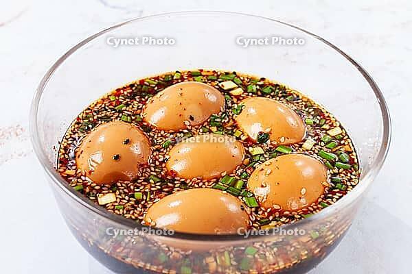 Five soft boiled eggs sit in a bowl filled with soy sauce, chopped green onions, and sesame seeds [IBR124585357]