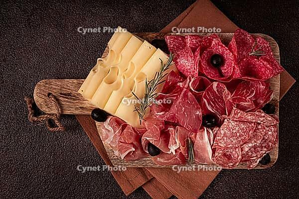 Assorted meat, appetizer, prosciutto, salami and ham, with maasdam cheese and olives, on a wooden board, breakfast, top view, close-up, no people [IBR124585360]