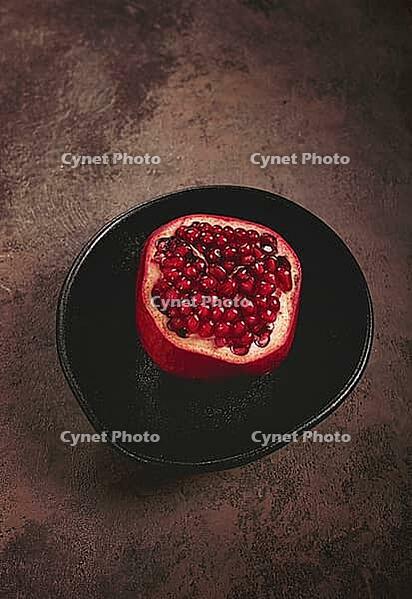 Sliced fresh pomegranate, on a black plate, top view, rustic style, no people [IBR124585366]