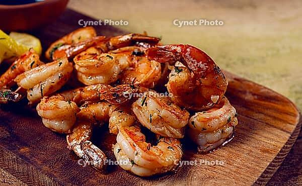 Fried tiger prawns, jumbo, in garlic sauce, in butter, with herbs, on a wooden board, homemade, no people [IBR124585368]
