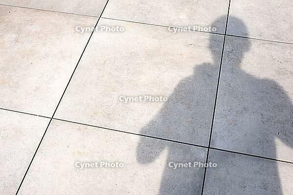 Person's shadow falling on light grey concrete pavement in bright sunlight [IBR124586567]