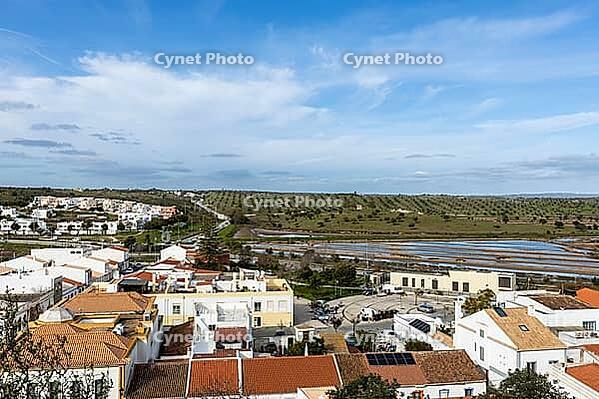 Wide panoramic view of Castro Marim showing traditional white houses with red roofs, streets, and surrounding countryside under a bright sky in the Algarve region of Portugal [IBR124586575]