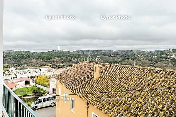 Panoramic view of São Marcos da Serra, a quiet rural village in the Algarve interior of Portugal, featuring traditional white houses, rolling green hills, and a cloudy sky [IBR124586583]