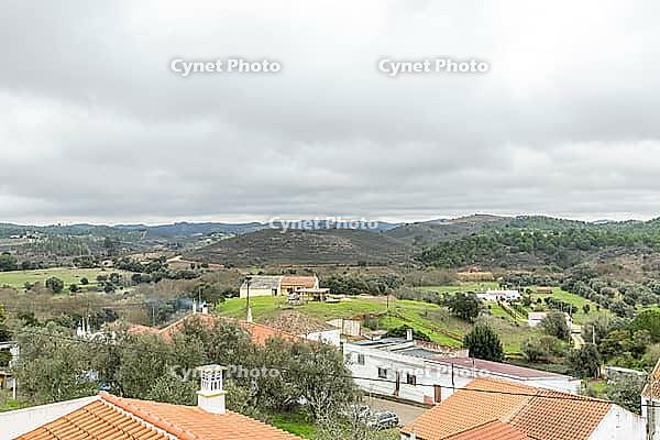 Panoramic view of São Marcos da Serra, a quiet rural village in the Algarve interior of Portugal, featuring traditional white houses, rolling green hills, and a cloudy sky [IBR124586591]