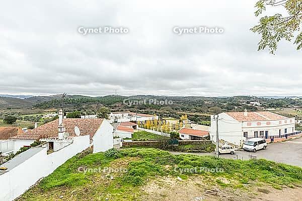 Panoramic view of São Marcos da Serra, a quiet rural village in the Algarve interior of Portugal, featuring traditional white houses, rolling green hills, and a cloudy sky [IBR124586596]