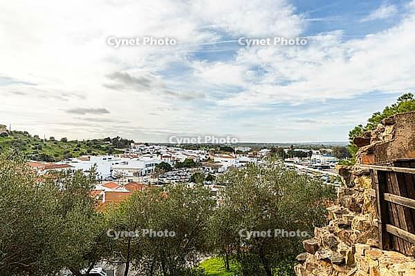 Wide panoramic view of Castro Marim showing traditional white houses with red roofs, streets, and surrounding countryside under a bright sky in the Algarve region of Portugal [IBR124586605]