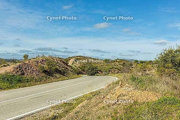 Scenic countryside road leading to Moinho das Amendoeiras in the Algarve, Portugal, surrounded by rolling hills, green landscape, and blue sky with clouds [IBR124586617]