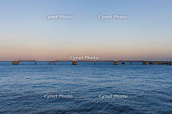 Peaceful seascape with gentle waves and a long pier stretching into the ocean at sunset in Lisbon, Portugal. Soft pastel sky and tranquil coastal atmosphere create a minimalist travel scene [IBR124586618]