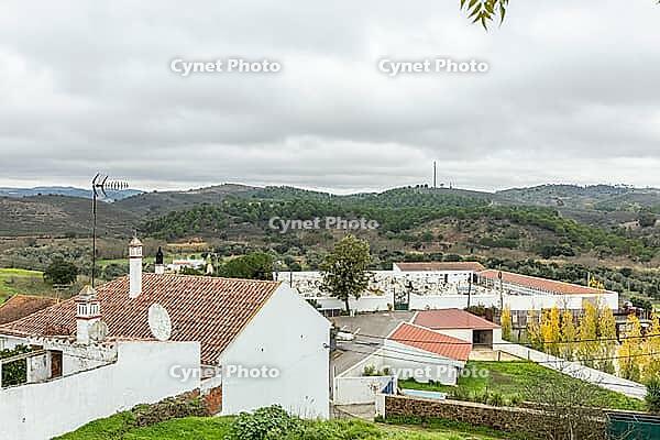 Panoramic view of São Marcos da Serra, a quiet rural village in the Algarve interior of Portugal, featuring traditional white houses, rolling green hills, and a cloudy sky [IBR124586627]
