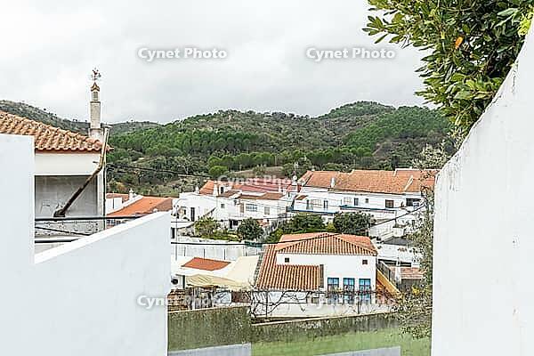 Panoramic view of São Marcos da Serra, a quiet rural village in the Algarve interior of Portugal, featuring traditional white houses, rolling green hills, and a cloudy sky [IBR124586629]